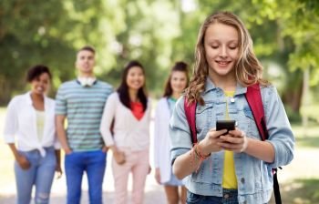 education, school and people concept - happy smiling teenage student girl with bag and smartphone over group of friends in summer park background. teen student girl with school bag and smartphone
