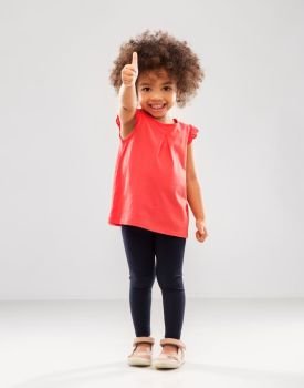 childhood, gesture and people concept - happy little african american girl showing thumbs up over grey background. little african american girl showing thumbs up