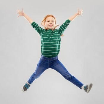 childhood, fashion and people concept - smiling red haired girl in green striped shirt and jeans jumping over grey background. smiling red haired girl in striped shirt jumping