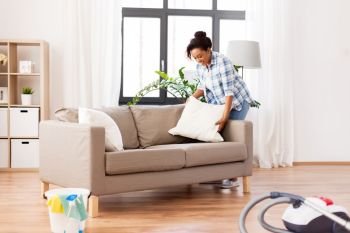 household, housework and cleaning concept - african american woman arranging sofa cushions at home. african american woman arranging sofa cushions