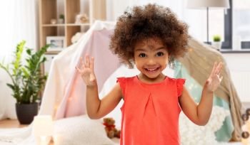 childhood and people concept - happy little african american girl over kids tent or teepee at home background. happy little african american girl at home