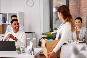 business, new job and quit concept - happy smiling colleagues looking at businesswoman or female employee holding her personal stuff at office. happy employee with personal stuff at office