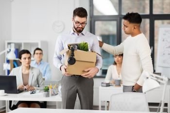 business, firing and job loss concept - colleague seeing off sad fired indian male office worker holding box of his personal stuff. colleague seeing off sad fired male office worker