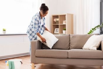 household, housework and cleaning concept - african american woman arranging sofa cushions at home. african american woman arranging sofa cushions