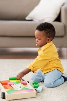 childhood, kids and people concept - lovely african american baby boy playing with wooden toy blocks kit on floor at home. african american baby boy playing with toy blocks