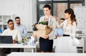 business, firing and job loss concept - colleague seeing off sad fired female employee with box of her personal stuff leaving office. female office worker with box of personal stuff