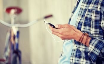 people, technology, leisure and lifestyle - close up of young hipster man with earphones, smartphone and bicycle listening to music. man with earphones and smartphone listening music