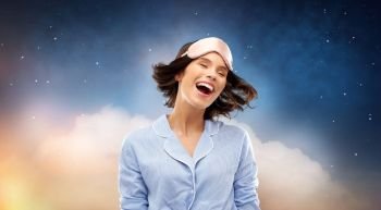 people and bedtime concept - happy young woman in pajama and eye sleeping mask over starry night sky and cloud background. happy young woman in pajama and eye sleeping mask