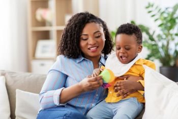 childhood, kids and people concept - happy african american mother and her baby son playing with ball together on sofa at home. mother and baby playing with ball at home