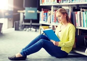 education, high school, university, learning and people concept - smiling student girl reading book sitting on floor at library. high school student girl reading book at library