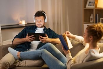leisure and people concept - couple with tablet computer, headphones and book at home in evening. couple with tablet computer and book at home