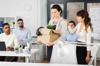 business, firing and job loss concept - colleague seeing off sad fired female employee with box of her personal stuff leaving office. female office worker with box of personal stuff