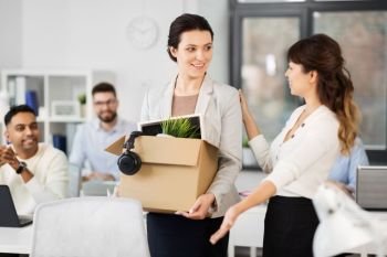 business, job and quit concept - new female office worker with box of personal stuff and happy smiling colleague. new female employee meeting colleagues at office