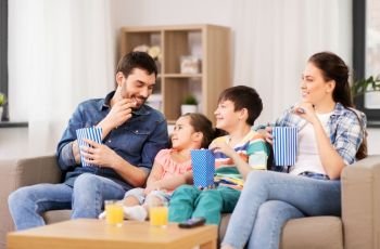 family, leisure and people concept - happy mother, father, son and daughter with popcorn watching tv at home. happy family with popcorn watching tv at home