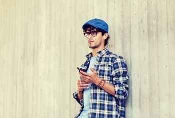 people, music, technology, leisure and lifestyle - happy young hipster man with earphones and smartphone listening to music. man with earphones and smartphone listening music