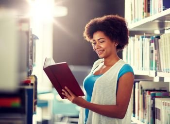 education, high school, university, learning and people concept - happy smiling african american student girl reading book at library. happy african student girl reading book at library