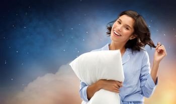 people and bedtime concept - happy young woman in pajama hugging pillow over starry night sky and cloud background. happy woman in pajama with pillow over night sky