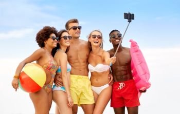 friendship, summer holidays and people concept - group of happy friends wit ball and mattress taking picture by smartphone on selfie stick on beach. happy friends taking selfie on summer beach