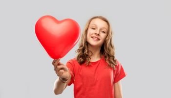 valentine’s day, love and people concept - smiling pretty teenage girl with long hair in red t-shirt holding heart shaped balloon over grey background. smiling teenage girl with red heart shaped balloon