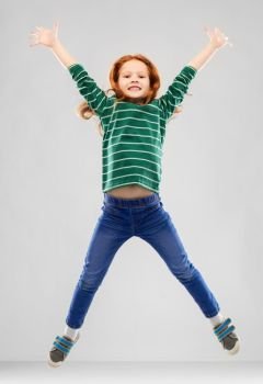 childhood, fashion and people concept - smiling red haired girl in green striped shirt and jeans jumping over grey background. smiling red haired girl in striped shirt jumping