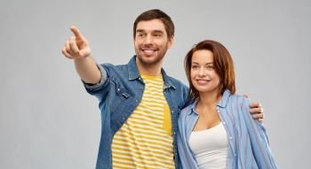 future planning, relationships and people concept - happy couple pointing finger to something over grey background. happy couple hugging