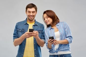 technology and people concept - happy couple using smartphones over grey background. happy couple using smartphones over grey