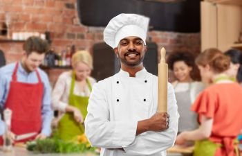 cooking class, profession and people concept - happy male indian chef or baker in toque with rolling-pin over group of students background. male indian chef with rolling-pin at cooking class