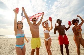 summer, holidays and people concept - group of happy friends with flag and non-alcoholic drinks celebrating american independence day and party on beach. friends at american independence day beach party