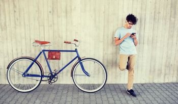people, communication, technology, leisure and lifestyle - hipster man with smartphone and earphones on fixed gear bike listening to music on city street. man with smartphone and earphones on bicycle
