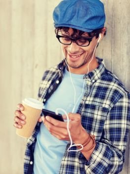 people, technology, leisure and lifestyle - close up of happy smiling man with earphones and smartphone drinking coffee and listening to music on city street. man with earphones and smartphone drinking coffee