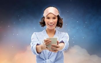 people and bedtime concept - happy young woman in pajama and eye sleeping mask drinking coffee from mug over background. woman in pajama and sleeping mask drinking coffee