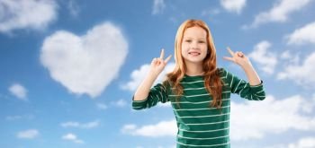 childhood, gesture and valentine’s day concept - smiling red haired girl in green striped shirt showing peace over blue sky and heart shaped cloud clouds background. smiling red haired girl showing peace over sky