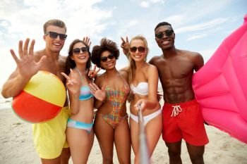 friendship, summer holidays and people concept - group of happy friends taking picture by selfie stick on beach. happy friends taking selfie on summer beach