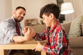 family, fatherhood and people concept - happy smiling father and little son arm wrestling at home in evening. happy father and little son arm wrestling at home