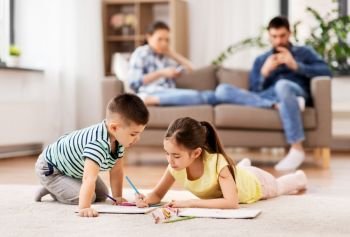 family, leisure and people concept - brother and sister lying on floor and drawing in sketchbooks with crayons at home. brother and sister drawing with crayons at home