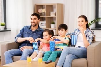 family, leisure and people concept - happy mother, father, son and daughter with popcorn watching tv at home. happy family with popcorn watching tv at home