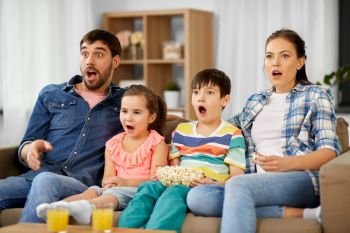 family, leisure and people concept - scared or surprised mother, father, son and daughter with popcorn watching horror on tv at home. scared family with popcorn watching horror on tv
