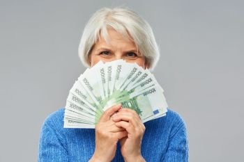 savings, finances and people concept - senior woman hiding face behind fan of hundred euro money banknotes. senior woman with hundreds of euro money banknotes