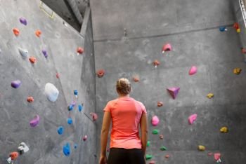 fitness, extreme sport, bouldering, people and healthy lifestyle concept - young woman at indoor climbing wall in gym from back. young woman at indoor climbing wall in gym