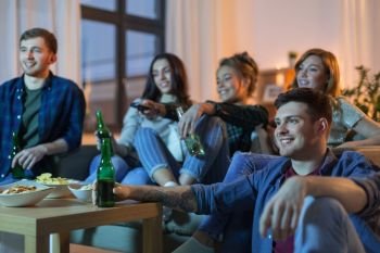 friendship and leisure concept - happy friends with non-alcoholic drinks watching tv at home in evening. happy friends with drinks watching tv at home