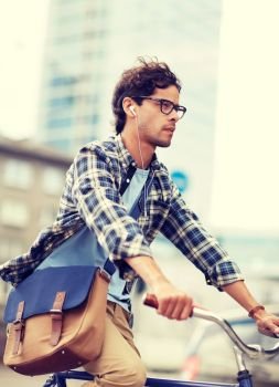 people, style, leisure and lifestyle - young hipster man with shoulder bag and earphones riding fixed gear bike on city street. young hipster man with bag riding fixed gear bike