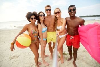 friendship, summer holidays and people concept - group of happy friends taking picture by selfie stick on beach. happy friends taking selfie on summer beach