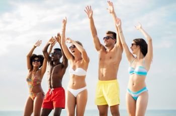 friendship, summer holidays and people concept - group of happy friends dancing with hands up having fun on beach. happy friends with hands up on summer beach