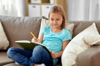 people, childhood and bedtime concept - little girl with diary and pencil sitting on sofa at home. little girl with diary sitting on sofa at home