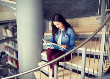 education, high school, university, learning and people concept - smiling student girl reading book sitting on stairs at library. high school student girl reading book at library