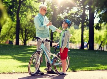 family, generation, safety and people concept - happy grandfather and boy with bicycle and bike helmet at summer park. grandfather and boy with bicycle at summer park