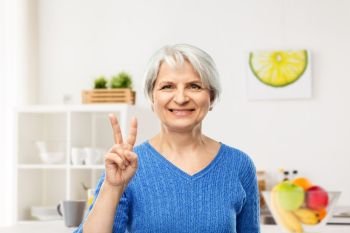 gesture and old people concept - portrait of smiling senior woman in blue sweater showing peace over kitchen background. smiling senior woman showing peace in kitchen