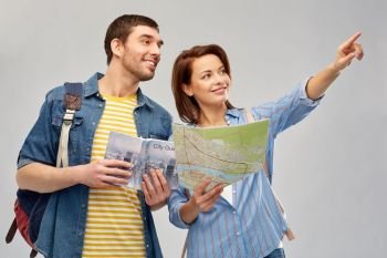 travel, tourism and vacation concept - happy couple of tourists with city guide, map and backpacks over grey background. happy couple of tourists with city guide and map