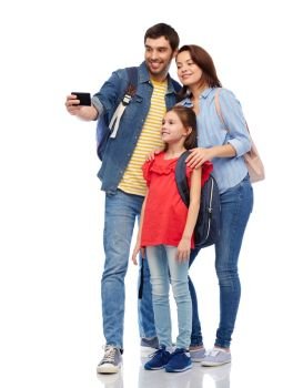family, tourism and travel concept - happy smiling mother, father and little daughter with backpacks taking selfie by smartphone over white background. happy family with backpacks taking selfie