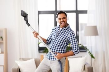 household and cleaning concept - indian man in headphones with vacuum cleaner having fun at home. man in headphones with vacuum cleaner at home